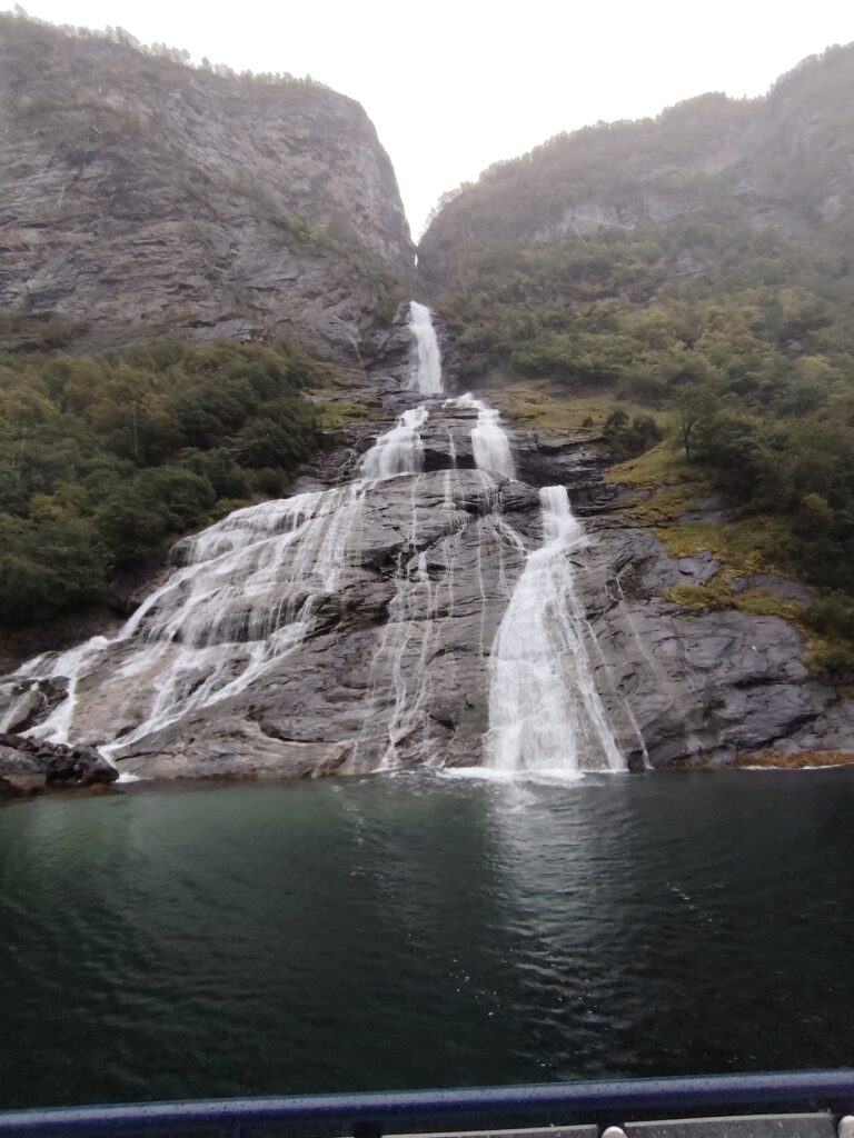 Das Bild zeigt einen Wasserfall in Norwegen vom Boot aus gesehen bei grauem Himmel.